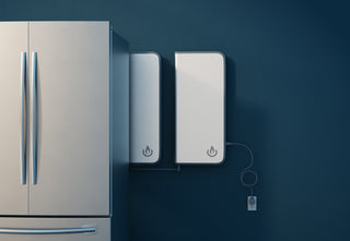 A home backup power device mounted on a wall next to a refrigerator, with a power symbol displayed on its front.